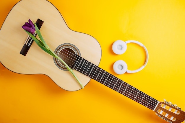 Chitarra bianca e cuffie wireless bianche su sfondo arancione, fiori primaverili, mazzo di tulipani viola, chitarra bianca e fiori, poster di musica primaverile.