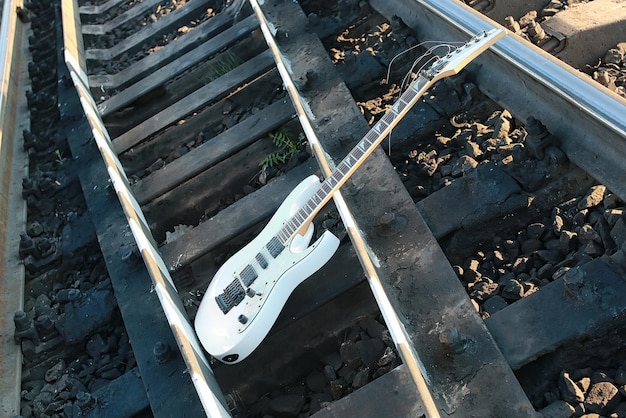 Chitarra elettrica bianca sui binari della ferrovia e pietra grigia industriale