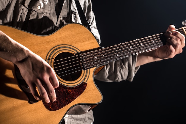 Chitarrista, musica. Un giovane suona una chitarra acustica su un muro nero isolato