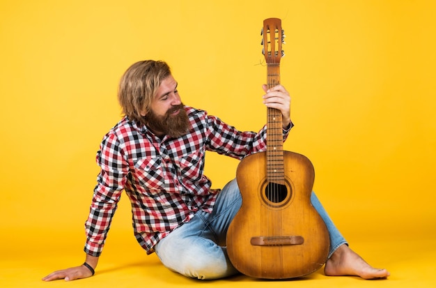 Chitarrista su sfondo giallo Chitarrista allegro carismatico uomo maturo a suonare la chitarra mentre è seduto rilassarsi con il ragazzo di musica preferito con la canzone che esegue la chitarra