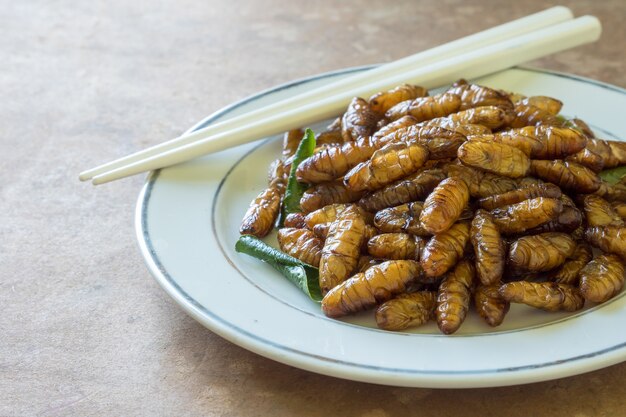 Chiuda in su degli insetti fritti nel piatto sulla tavola di legno.