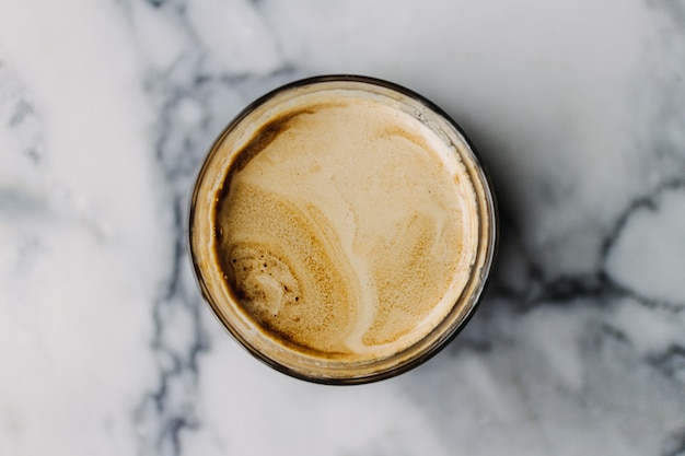 Chiuda in su del caffè Latte sporco con struttura in marmo sul caffè e sul tavolo.