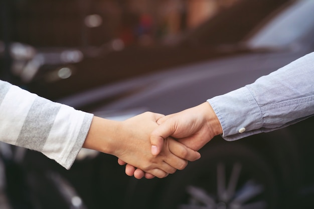 Chiuda in su del concessionario che dà la chiave al nuovo proprietario e si stringono la mano nel salone dell'auto o nel salone