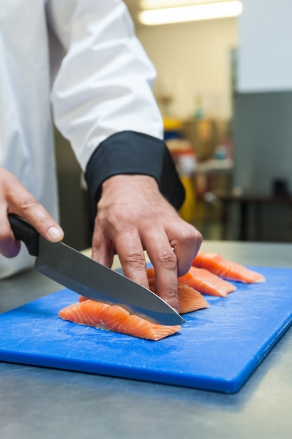Chiuda in su del cuoco unico che affetta il salmone crudo con il coltello affilato