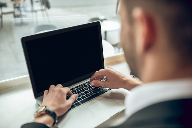 Chiuda in su del giovane uomo d'affari che lavora al computer portatile in un caffè