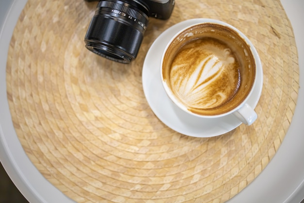 Chiuda in su del latte bianco sporco della tazza di caffè con arte di figura del cuore sulla tabella con la macchina fotografica