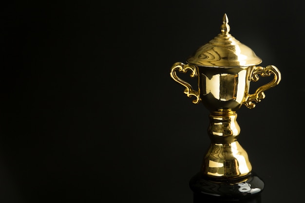 Chiuda in su del trofeo dorato sopra priorità bassa nera. Vincere premi con spazio copia per testo e design.