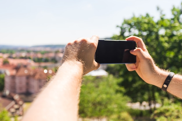 Chiuda in su del turista dell'uomo che prende foto con lo smartphone davanti alla città