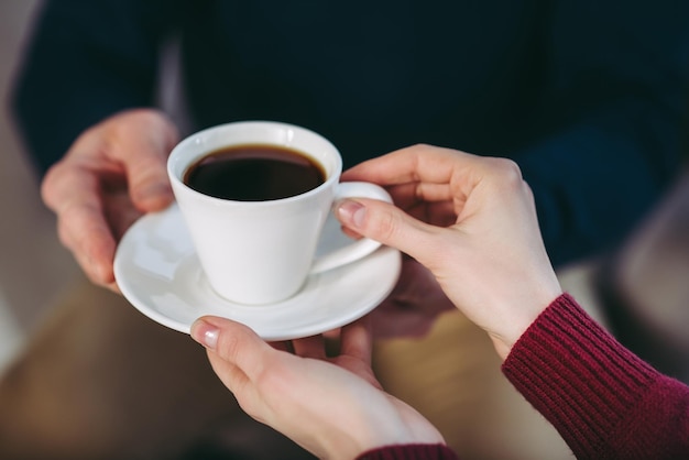 Chiuda in su dell'uomo che dà alla donna una tazza di caffè sul piatto