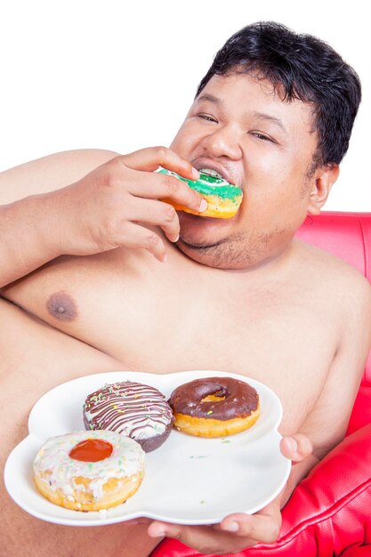 Chiuda in su dell'uomo grasso affamato mangiare ciambelle in studio
