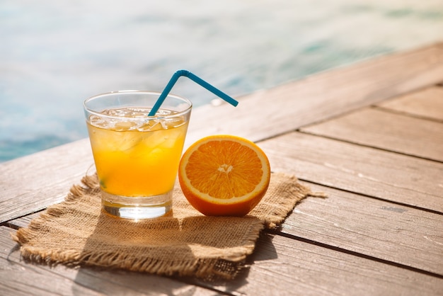 Chiuda in su della bevanda alcolica cocktail cacciavite con succo d'arancia, fette e ghiaccio in piedi vicino alla piscina. Bevanda rinfrescante di limonata ghiacciata in vetro a bordo piscina. I riflessi del sole. Sfondo, copia spazio.