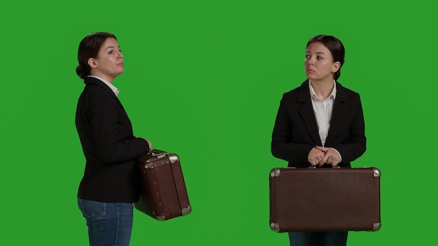 Chiuda in su della borsa della valigia di trasporto della donna d'affari in studio, in posa su sfondo greenscreen. Dipendente donna che tiene valigetta e bagagli sulla macchina fotografica, preparandosi per il viaggio con borse da viaggio.