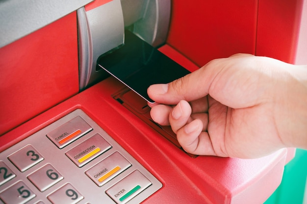 Chiuda in su della carta di bancomat di inserzione di mano di uomo in macchina di cassiere automatizzata per prelevare contanti mone