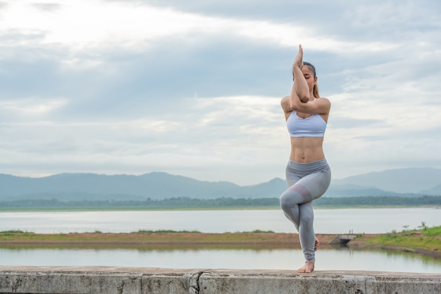 Chiuda in su della donna asiatica che fa posa di yoga in spiaggia.