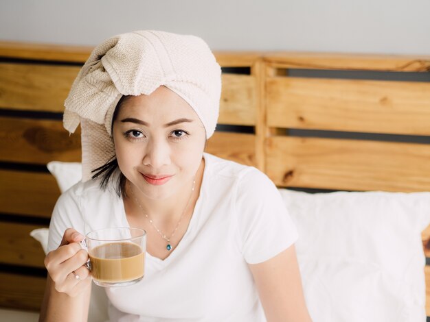 Chiuda in su della donna bere il caffè del mattino e rilassarsi sul suo letto dopo la doccia.