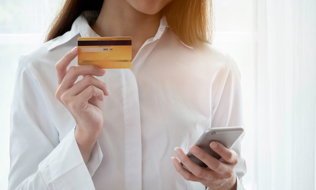 Chiuda in su della donna felice di utilizzare la carta di credito e smartphone per pagare per l&#39;acquisto online