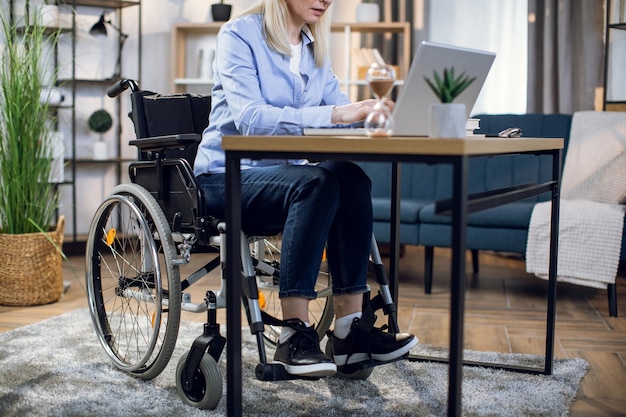 Chiuda in su della donna in sedia a rotelle che lavora al computer portatile