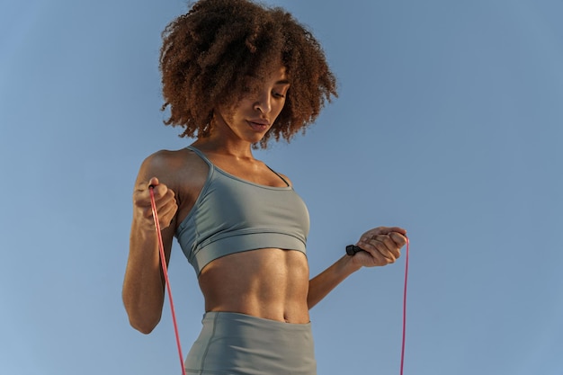 Chiuda in su della donna in treni di abbigliamento sportivo con corda per saltare su forza e motivazione di sfondo dello studio