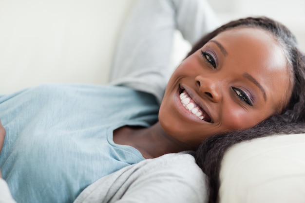 Chiuda in su della donna sorridente prendendo un riposo sul divano