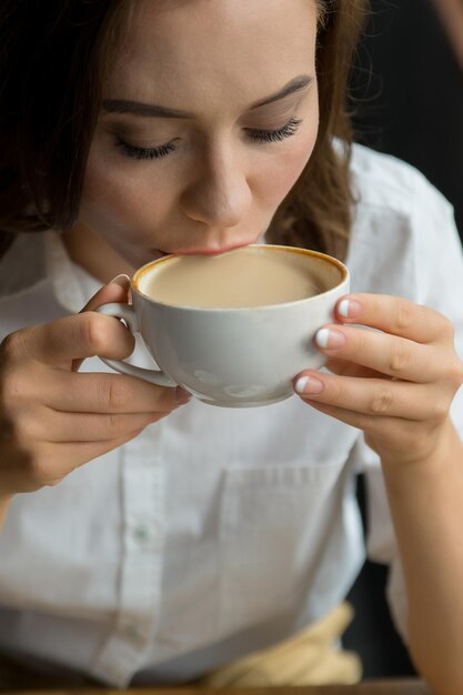 Chiuda in su della giovane bella donna che beve caffè in un caffè