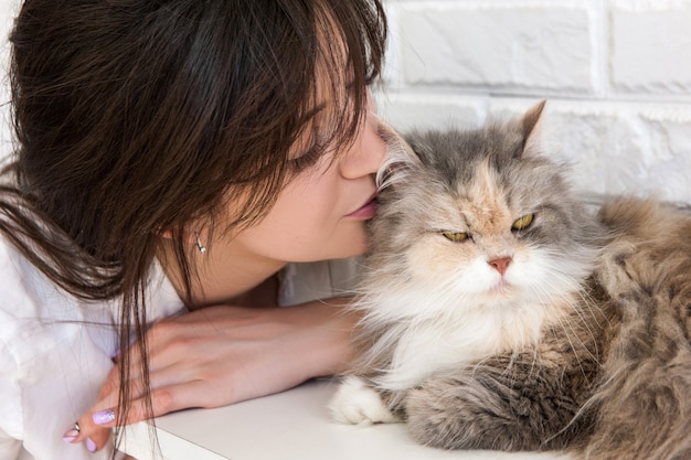 Chiuda in su della giovane donna bruna bacia il suo adorabile gatto. Affascinanti animali domestici e l'amore della gente per loro
