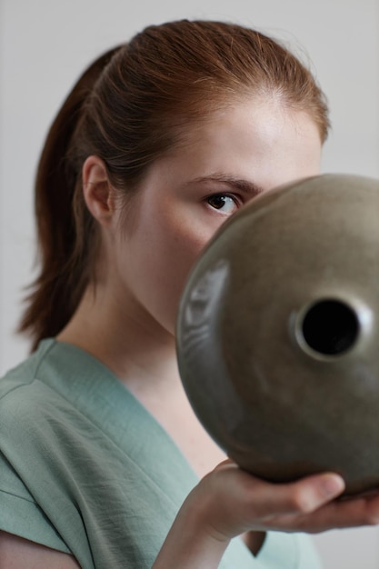 Chiuda in su della giovane donna che tiene vaso di ceramica fatto a mano