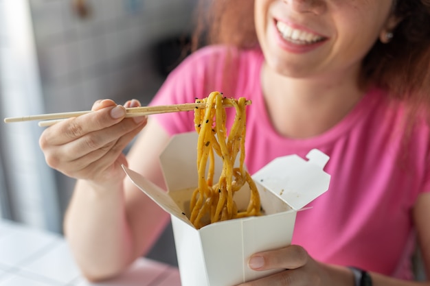 Chiuda in su della mano di una giovane ragazza non identificata che mangia tagliatelle cinesi con le bacchette di legno