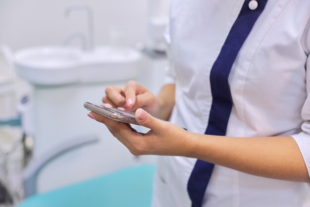 Chiuda in su della mano femminile del medico con lo smartphone del telefono mobile