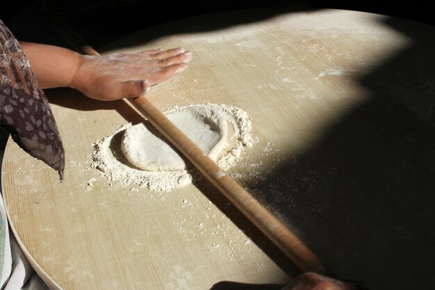 Chiuda in su della pasta di rotolamento della donna con il mattarello