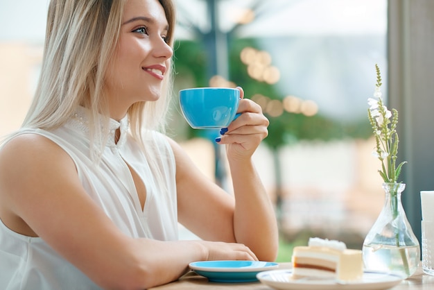 Chiuda in su della ragazza bionda sveglia che mantiene la tazza di caffè all'aperto, sorridendo.