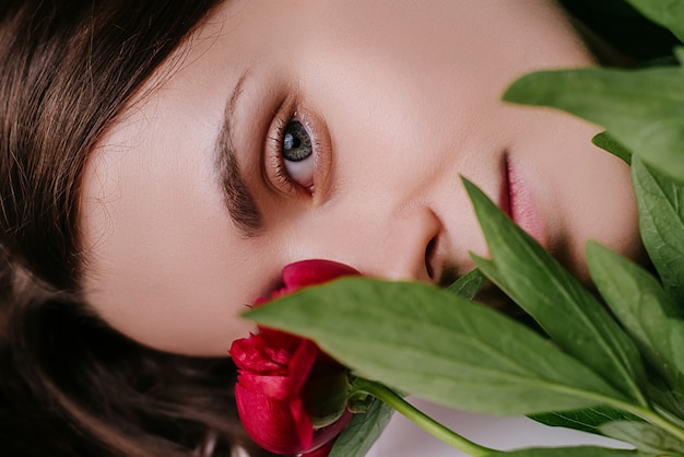 Chiuda in su della ragazza carina ritratto romantico con peonie rosse fresche e foglie verdi.