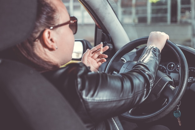 Chiuda in su della sigaretta di fumo della mano della donna all'interno dell'auto mentre si guida un veicolo