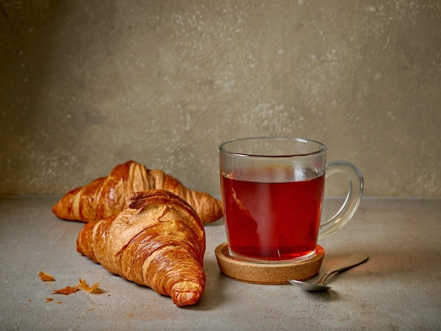 Chiuda in su della tazza di tè e dei croissant