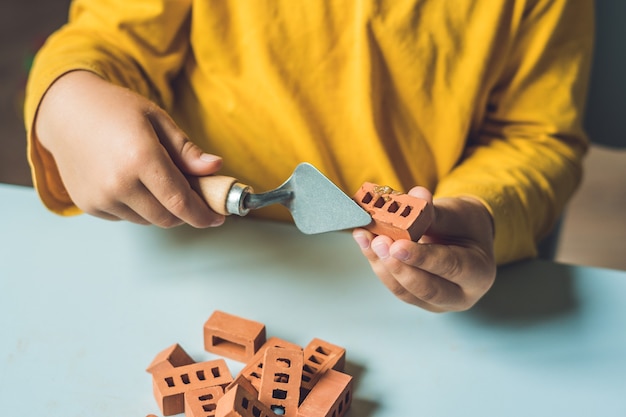 Chiuda in su delle mani del bambino che gioca con i piccoli mattoni di argilla reale al tavolo