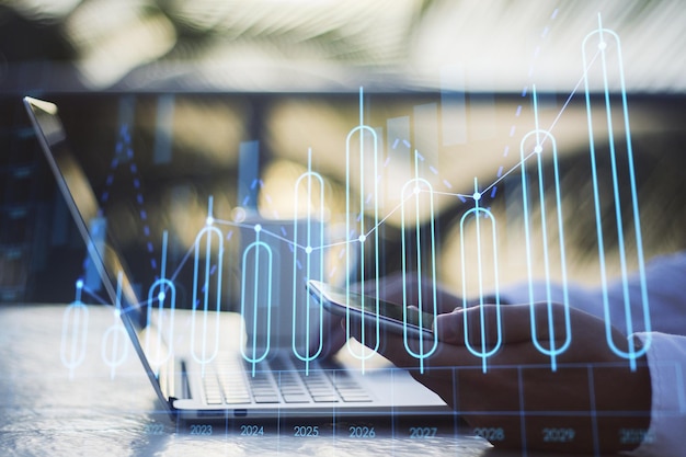 Chiuda in su delle mani dell'uomo d'affari utilizzando computer portatile e smartphone con grafico di business annuale in crescita