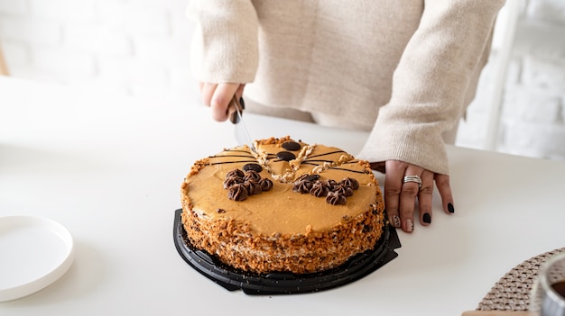 Chiuda in su delle mani della donna che tagliano la torta marrone