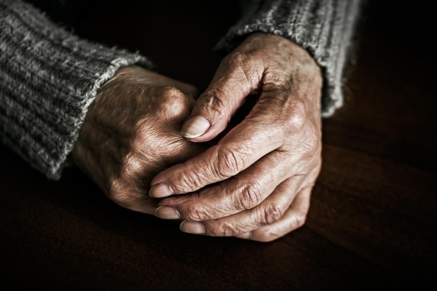 Chiuda in su delle mani della donna senior sul tavolo. Fotografia drammatica