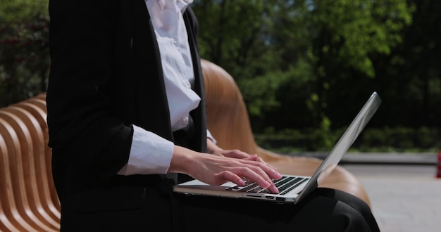 Chiuda in su delle mani della donna utilizzando il computer portatile all'aperto vicino all'edificio per uffici