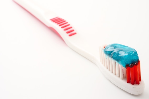 Chiuda in su dello spazzolino da denti con dentifricio in pasta su una priorità bassa bianca.