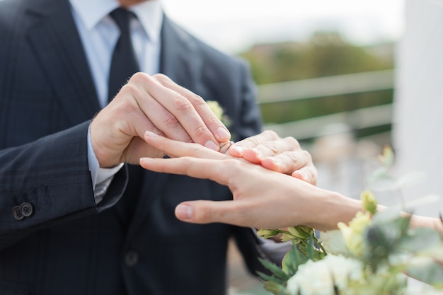 Chiuda in su dello sposo che mette l'anello dorato sul dito della sposa