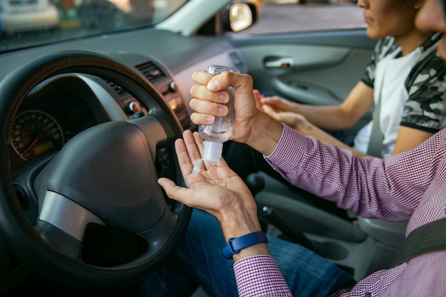 Chiuda in su di due uomini che applicano gel igienizzante alle sue mani all'interno della sua auto