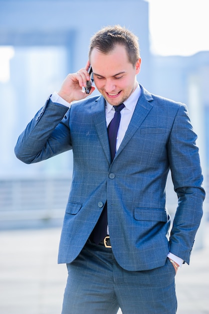 Chiuda in su di giovane uomo d'affari che cammina vicino all'aeroporto moderno. Parlando con il telefono. Vestito classico.