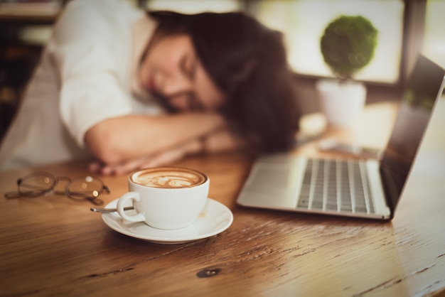 Chiuda in su di pieno di caffè in tazza di caffè con la donna di affari stanco dal lavoro