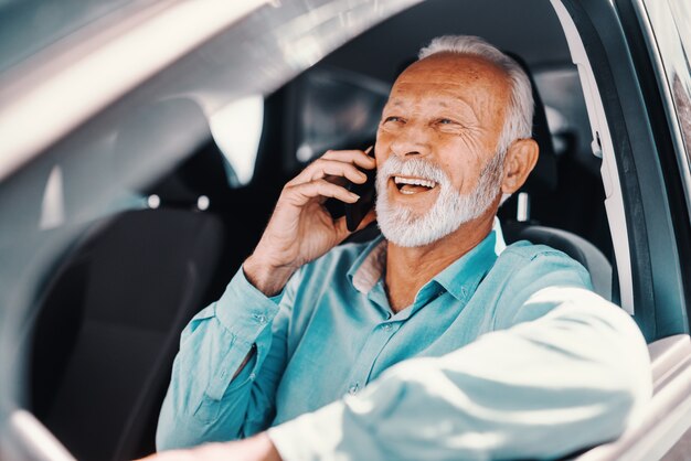 Chiuda in su di sorridere barbuto senior parlando al telefono con il braccio sulla finestra aperta mentre era seduto in macchina.