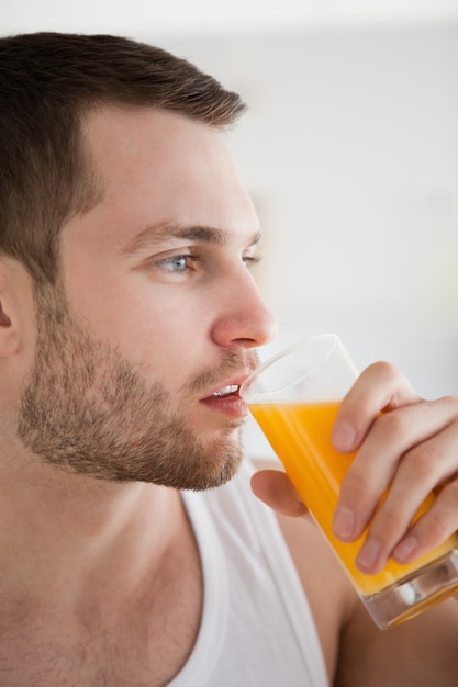 Chiuda in su di un giovane che beve il succo di arancia