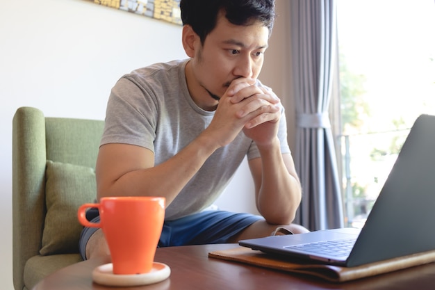 Chiuda in su di un uomo asiatico serio che lavora al suo computer portatile nella caffetteria.