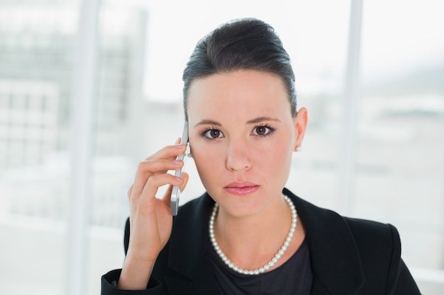 Chiuda in su di una donna di affari elegante seria che per mezzo del cellulare