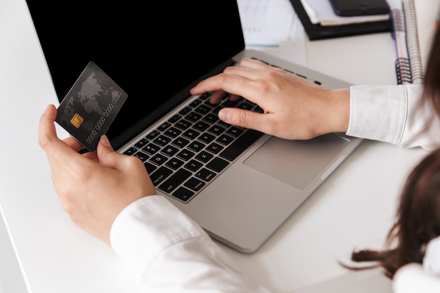 Chiuda in su di una donna in camicia bianca che si siede con il computer portatile