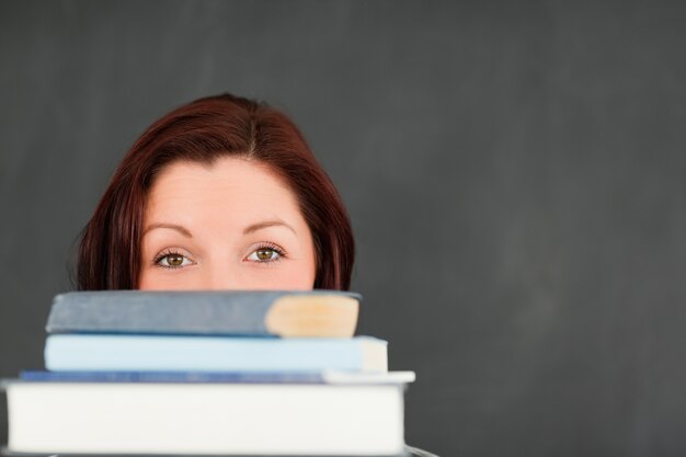 Chiuda in su di una giovane donna che si nasconde dietro una pila di libri