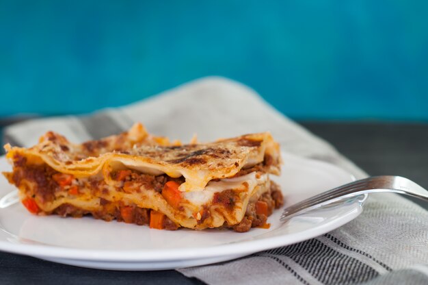 Chiuda in su di una lasagna tradizionale fatta con salsa bolognese di manzo servita su un piatto bianco